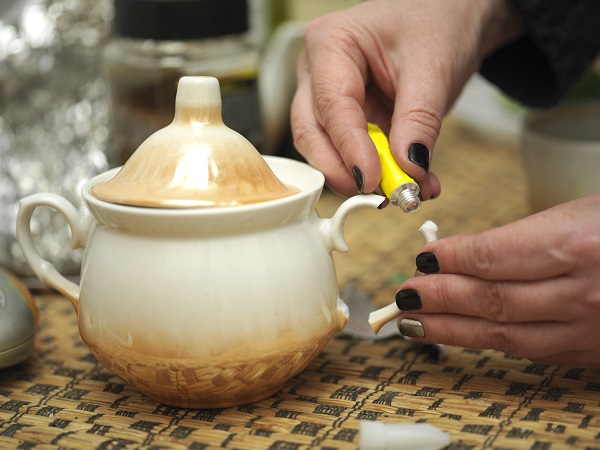 Manicured female hands gluing a broken sugar bowl, macro shot
