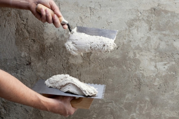 construction notched trowel and worker hands with white mortar on wall