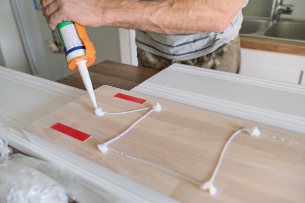 Carpenter male using construction glue when working with wooden white painted board, closeup, carpentry, woodwork, profession, people.