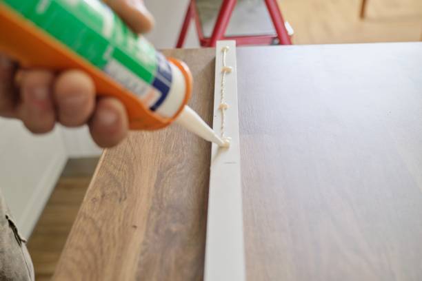 Carpenter male using construction glue when working with wooden white painted board, closeup, carpentry, woodwork, profession, people