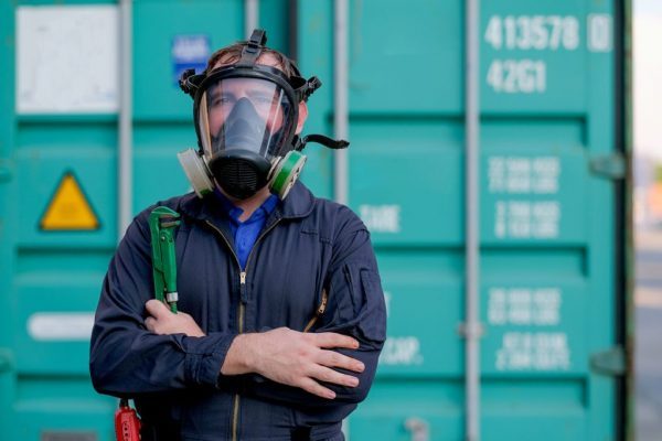 Technician or worker with chemical mask stand and hold wrench in front of green container and look confident.