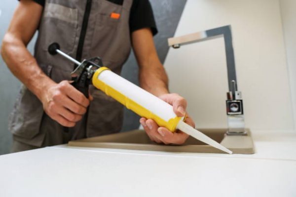 worker seals kitchen sink with sealant. hands of worker works with construction sealant gun in the kitchen