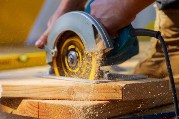 Carpenter using circular saw cutting wooden boards with hand power tools.