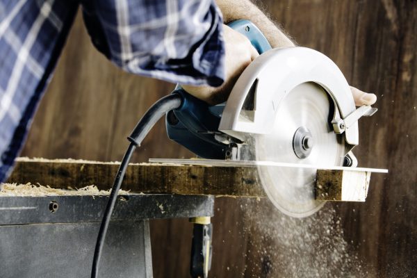 male-carpenter-using-electric-circular-saw-in-home-workshop-with-wood-chips-flying-926602156-5c56243646e0fb0001c089cc