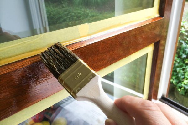 Man repaint a window frame with brown varnish