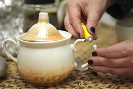 Manicured female hands gluing a broken sugar bowl, macro shot