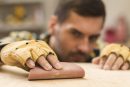close-up-of-male-carpenter-wearing-protective-gloves-in-hand-rubbing-sandpaper-on-wooden-plank
