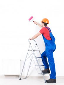 Craftsman painter stands on the stairs with roller, full portrait over white background , rear view