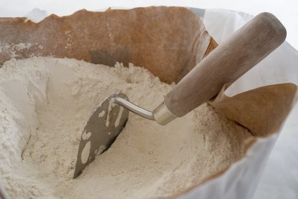 Close-up of plaster trowel in full open paper bag of putty powder for wall decoration,caulk or glaze.Concept of building materials.Finish coating in dry cement powder form.Selective focus,copy space